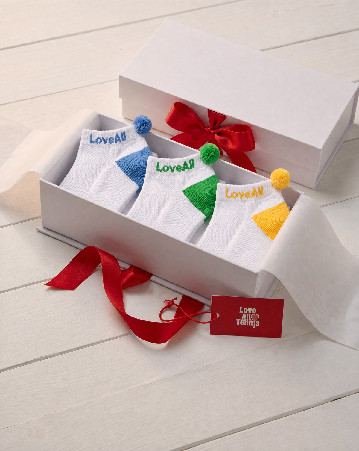 Set of colorful socks with pom-poms in a gift box on a light wooden surface